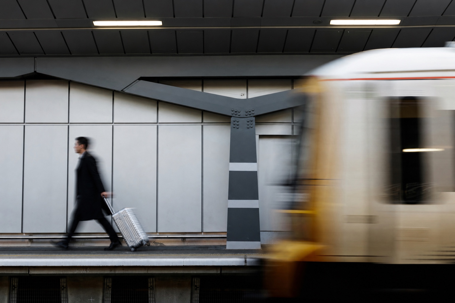 Male traveler pulling an aluminum suitcase through a station