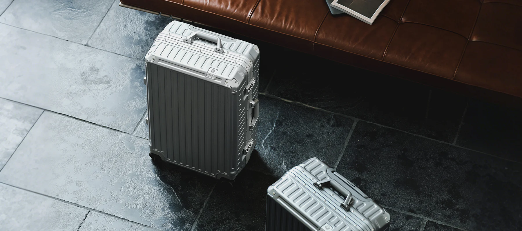 Silver aluminum luggage beside a leather sofa